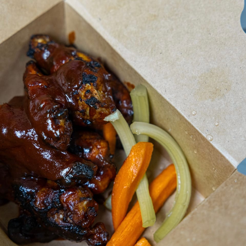BBQ chicken wings with carrots and celery sticks in a brown takeout box.