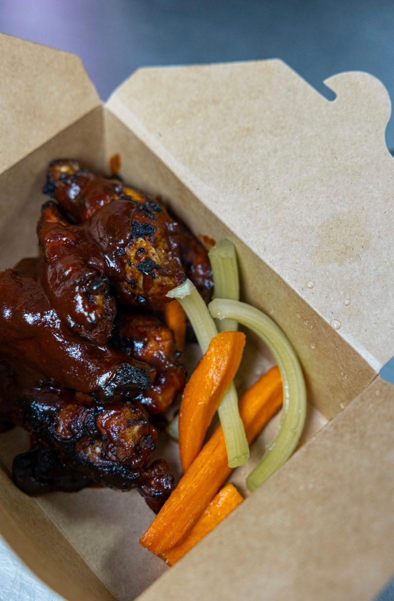 BBQ chicken wings with carrots and celery sticks in a brown takeout box.