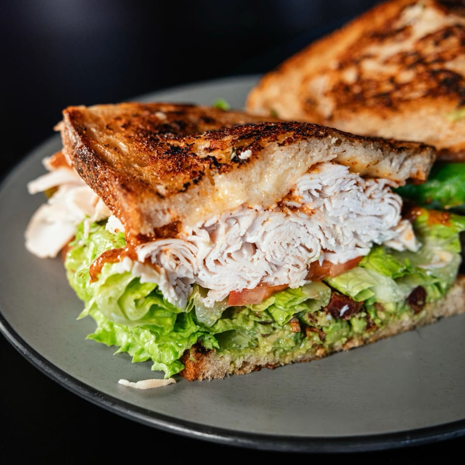 Grilled sandwich with turkey, lettuce, tomato, and guacamole on a gray plate.
