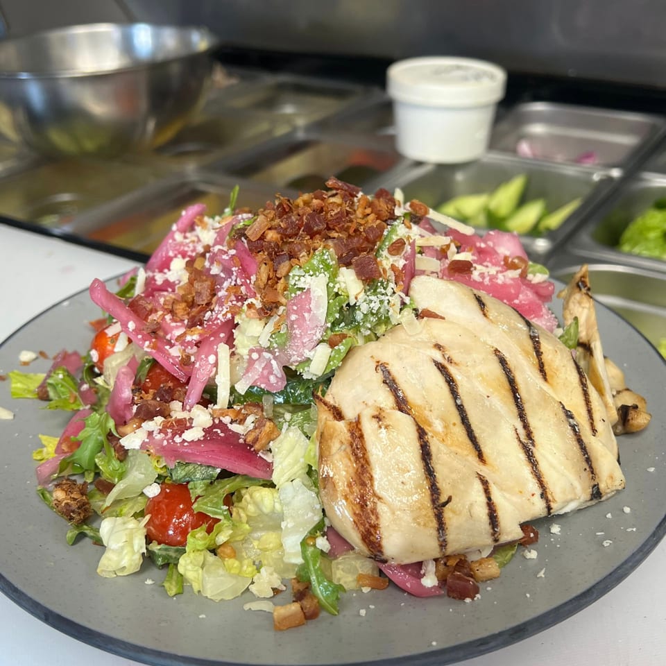 Grilled chicken salad with lettuce, tomatoes, pickled onions, bacon, and cheese.