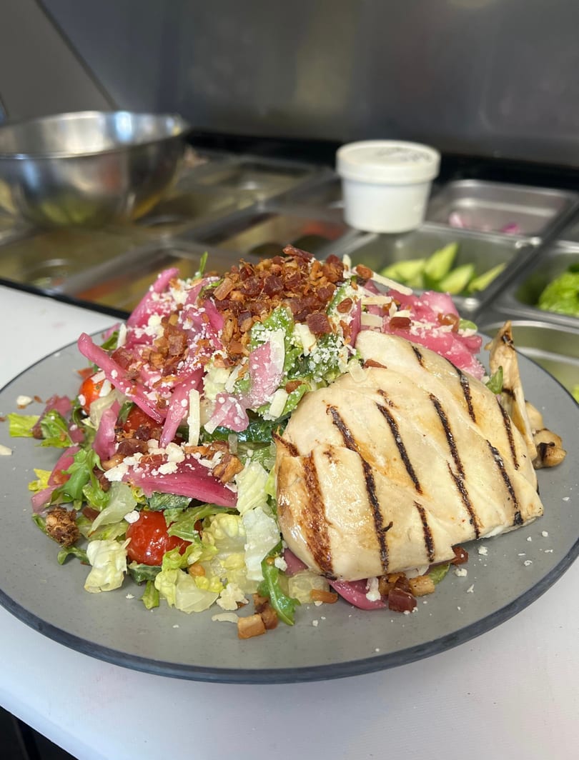 Grilled chicken salad with lettuce, tomatoes, pickled onions, bacon, and cheese.