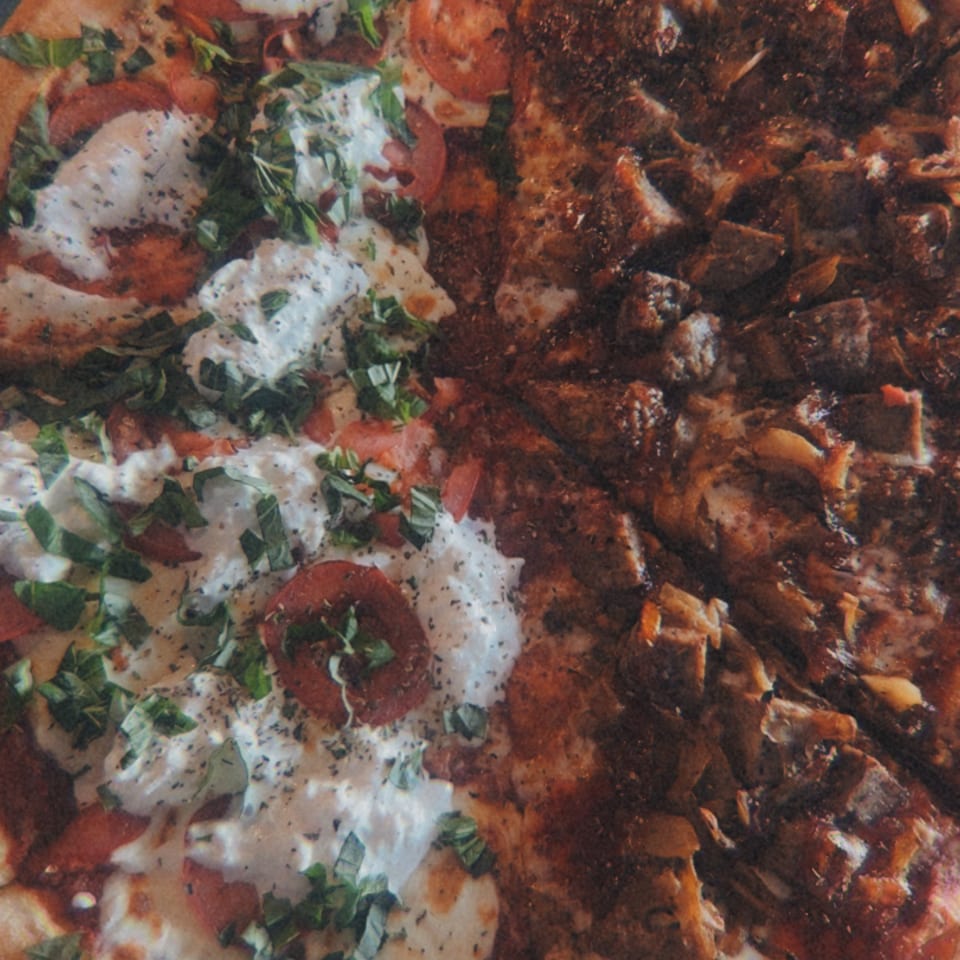 Close-up of a half-and-half pizza with fresh mozzarella, tomatoes, and basil on one side, and meat on the other.